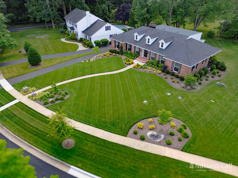 Aerial view of the completed Greenville, Delaware landscape transformation, brick lamp pillar entry, curved walkway, layered front beds, and natural stone retaining wall by Nature's Call Landscaping