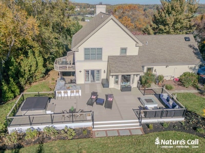 Large composite deck spans two levels with metal railings, fire pit, seating areas, and foundation plantings bordering contemporary home.