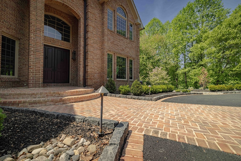 Hockessin Delaware estate front entry: brick paver walkway with herringbone pattern leading to the front door, flanked by stone-edged planting beds, Nature's Call Landscaping hardscaping project.