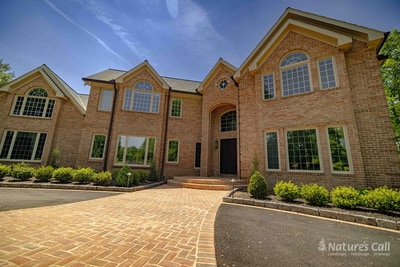 Detail view of the Hockessin entry walkway: a curved cobble edge defines the boundary between the brick paver path and a mulched bed of mounded boxwoods, with the brick step landing visible at the top of the frame
