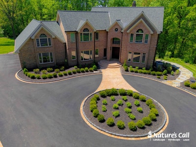Grand brick estate in Hockessin, DE with curved driveway, circular ornamental grass island, and low foundation plantings framing the entry.