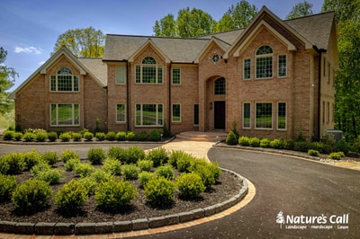 Modern brick colonial in Hockessin, DE with curved driveway bordered by boxwood foundation plantings and stone edging along landscaped beds.