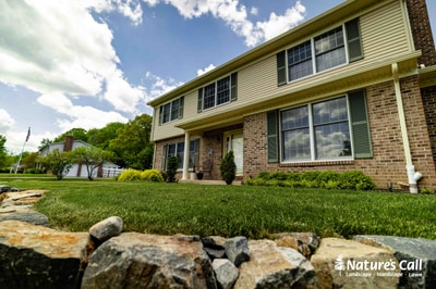 Natural stone retaining wall fronts a brick colonial with green lawn and foundation plantings in Garnet Valley, Pennsylvania.