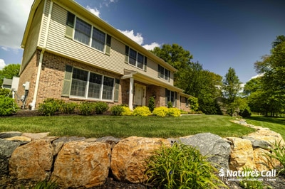 Stone retaining wall and manicured lawn with yellow flowering shrubs frame a contemporary brick home in Garnet Valley, Pennsylvania.
